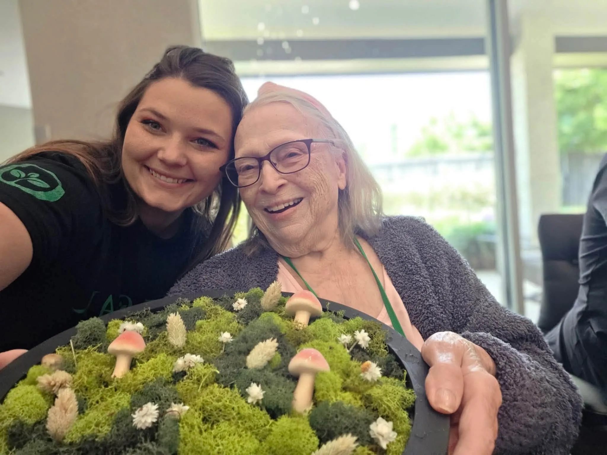 A caregiver and a smiling resident cheek to cheek at The Sage Oak of Colleyville