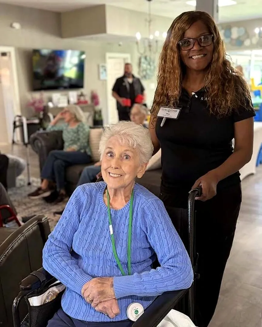 A caregiver beside a smiling resident at The Sage Oak of Colleyville